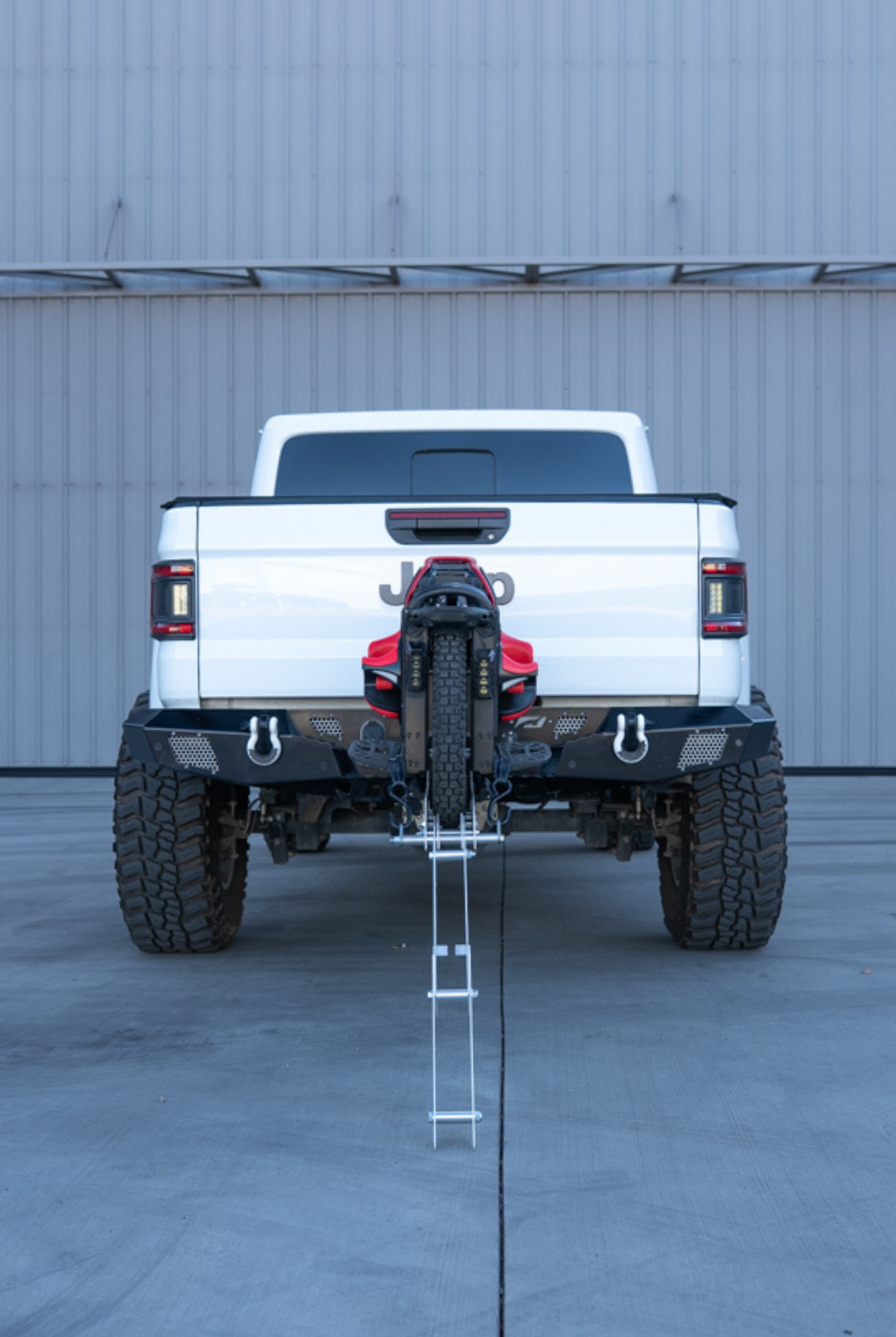 Lifted pickup truck hauling an electric unicycle on a hitch-mounted carrier with the ramp stowed for driving