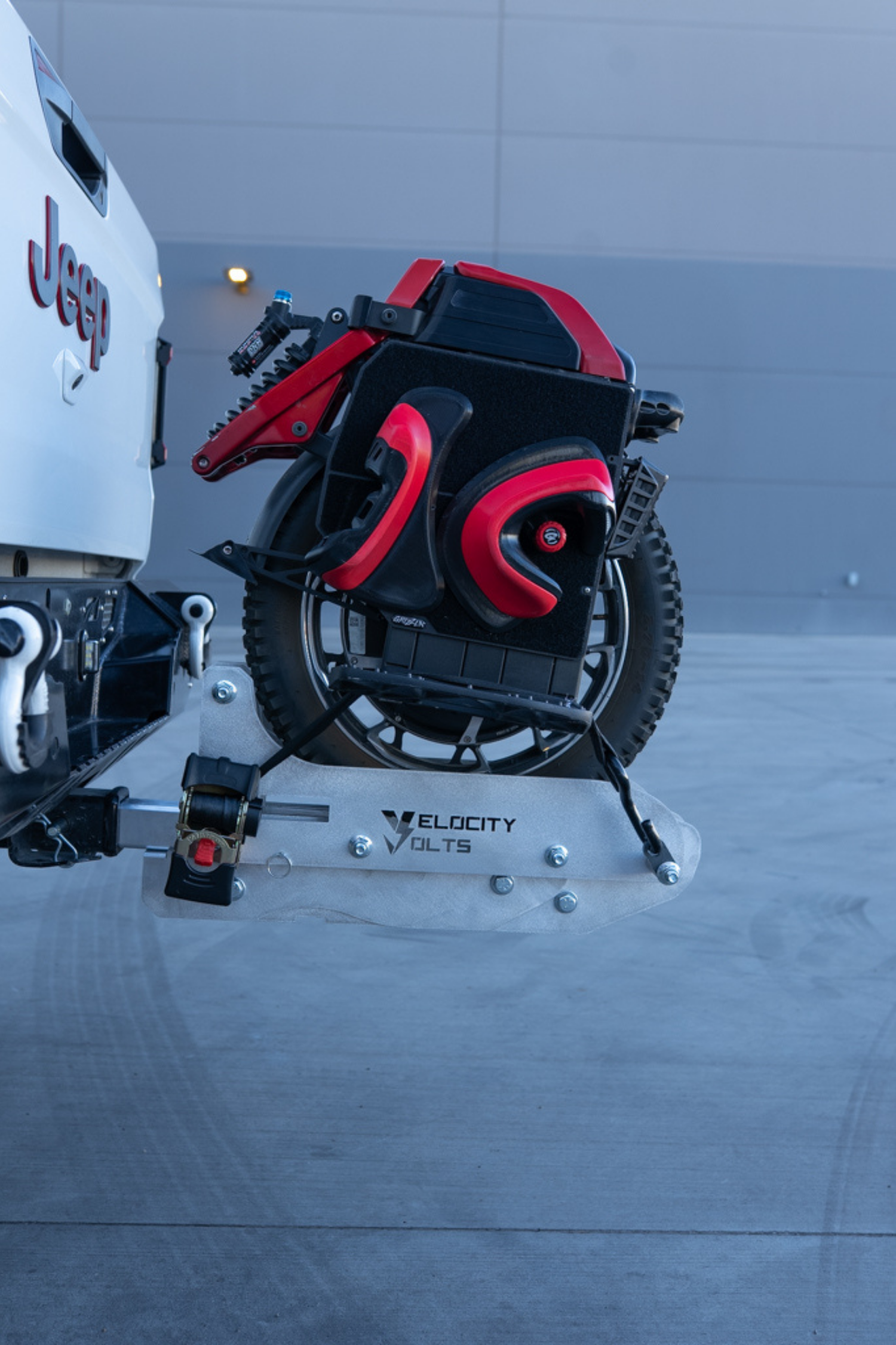 Side view of a PEV transport rack carrying an electric unicycle secured with a retractable ratchet strap