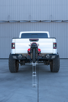 Lifted pickup truck hauling an electric unicycle on a hitch-mounted carrier with the ramp stowed for driving