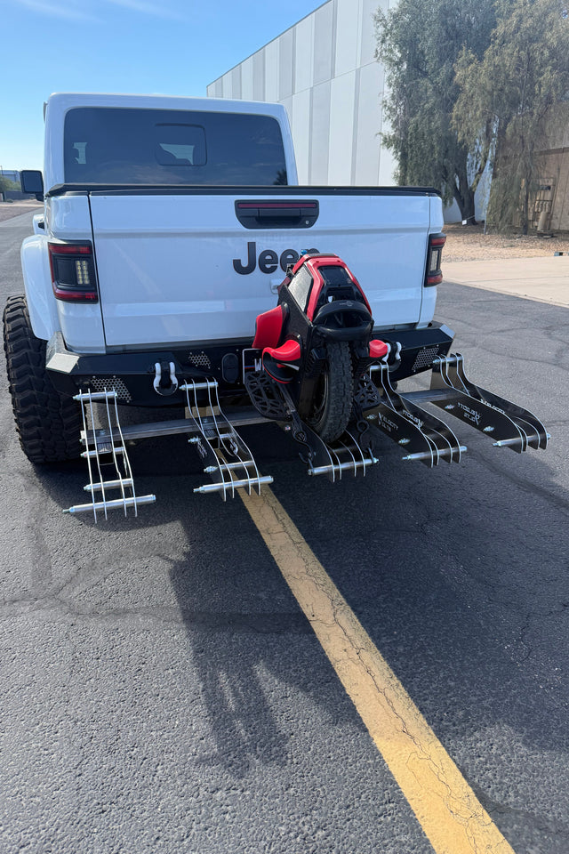 White Jeep vehicle with a large black and red off-road vehicle attached on a street.